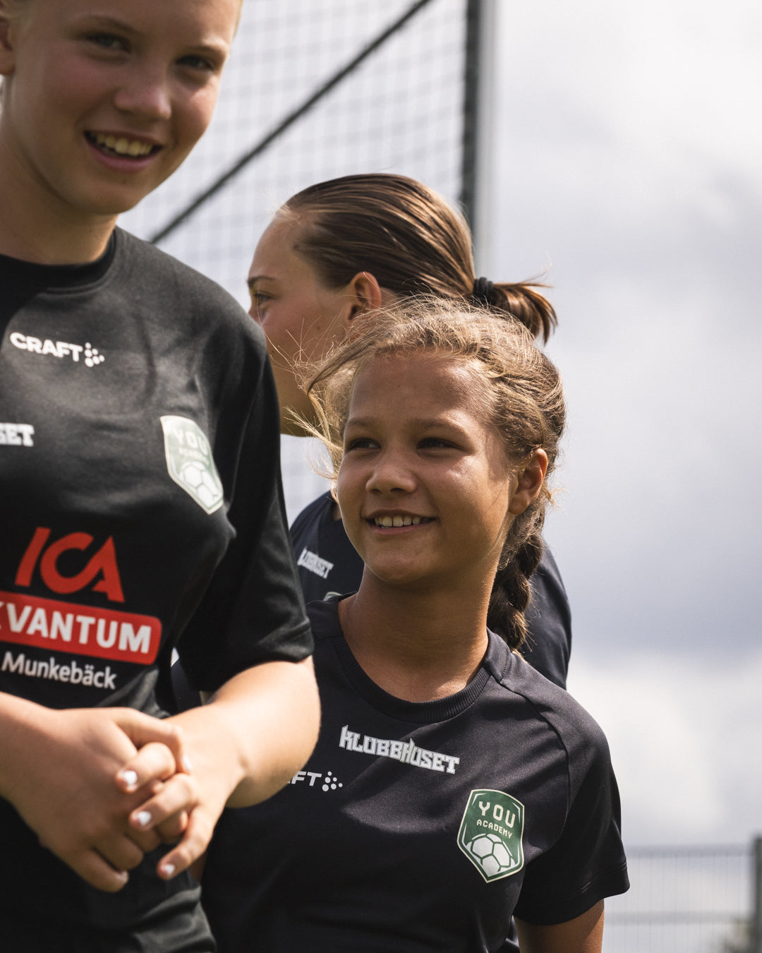 Two young women in sports jerseys shaking hands with a third person, outdoors.