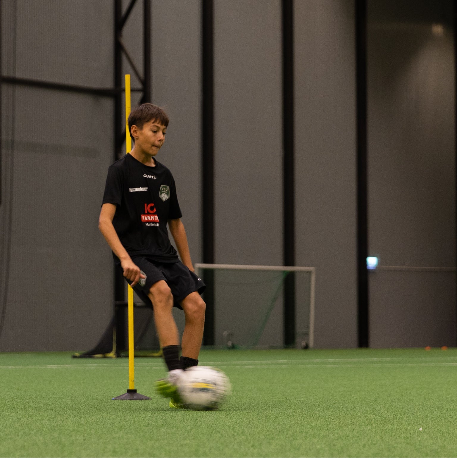 Child playing with a soccer ball on a green field with a dark background